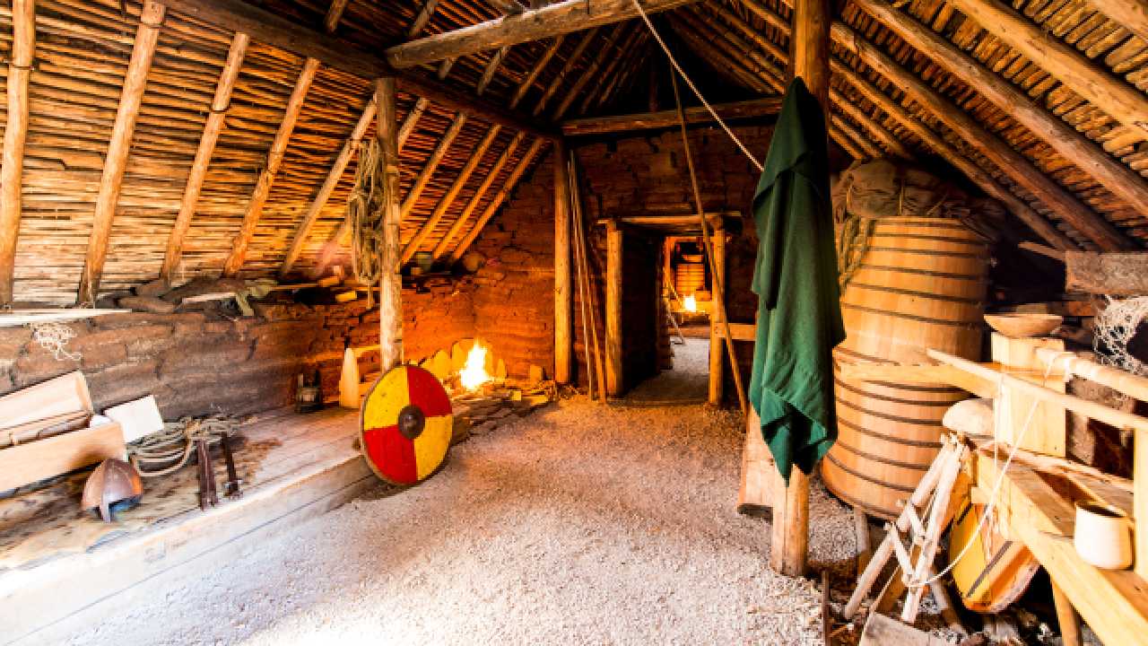 Inside of a Viking building with a fire, shield and other Viking objects